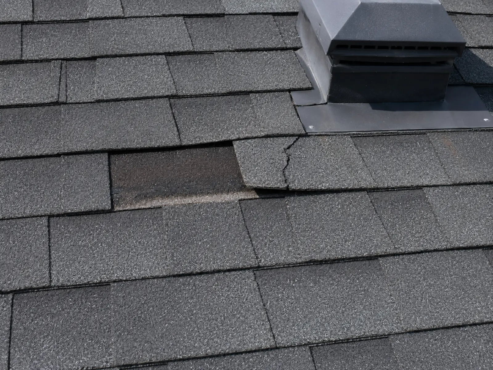 Missing, lifted and cracked asphalt shingles near a roof vent